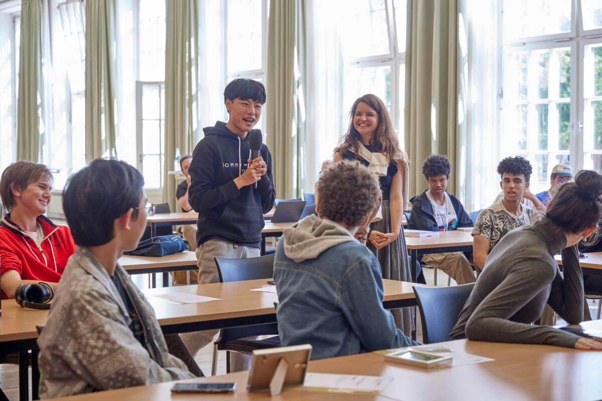 A student holds a microphone, other students listen to him